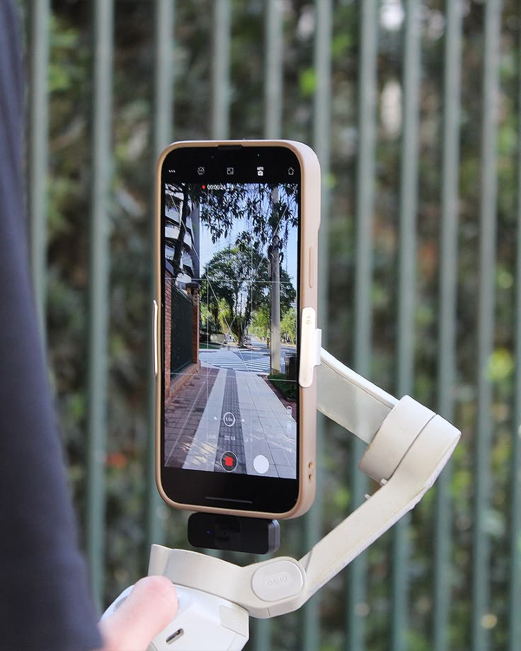 "Primer plano de un teléfono inteligente montado en un estabilizador gimbal Osmo, grabando una toma exterior fluida con cuadrícula de composición en pantalla, representando la producción audiovisual profesional y de alta calidad técnica realizada por 3videoweb."
